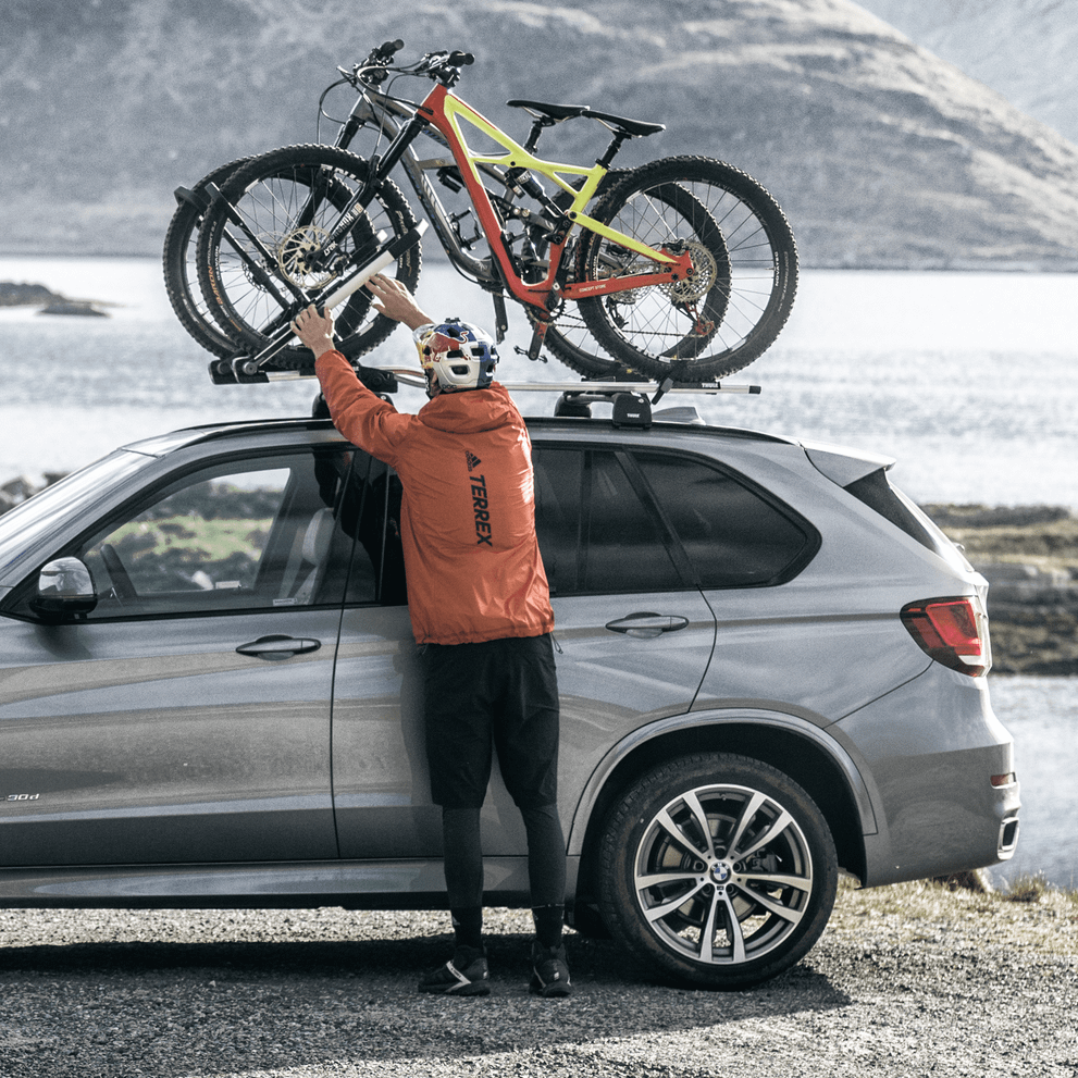 A car is parked by a lake with bikes mounted on a Thule UpRide.