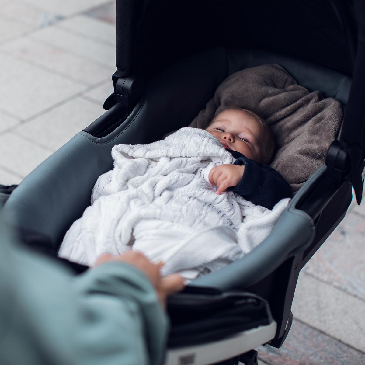 A close-up of a baby sleeping with a blanket inside a black Thule Urban Glide 2 baby bassinet.