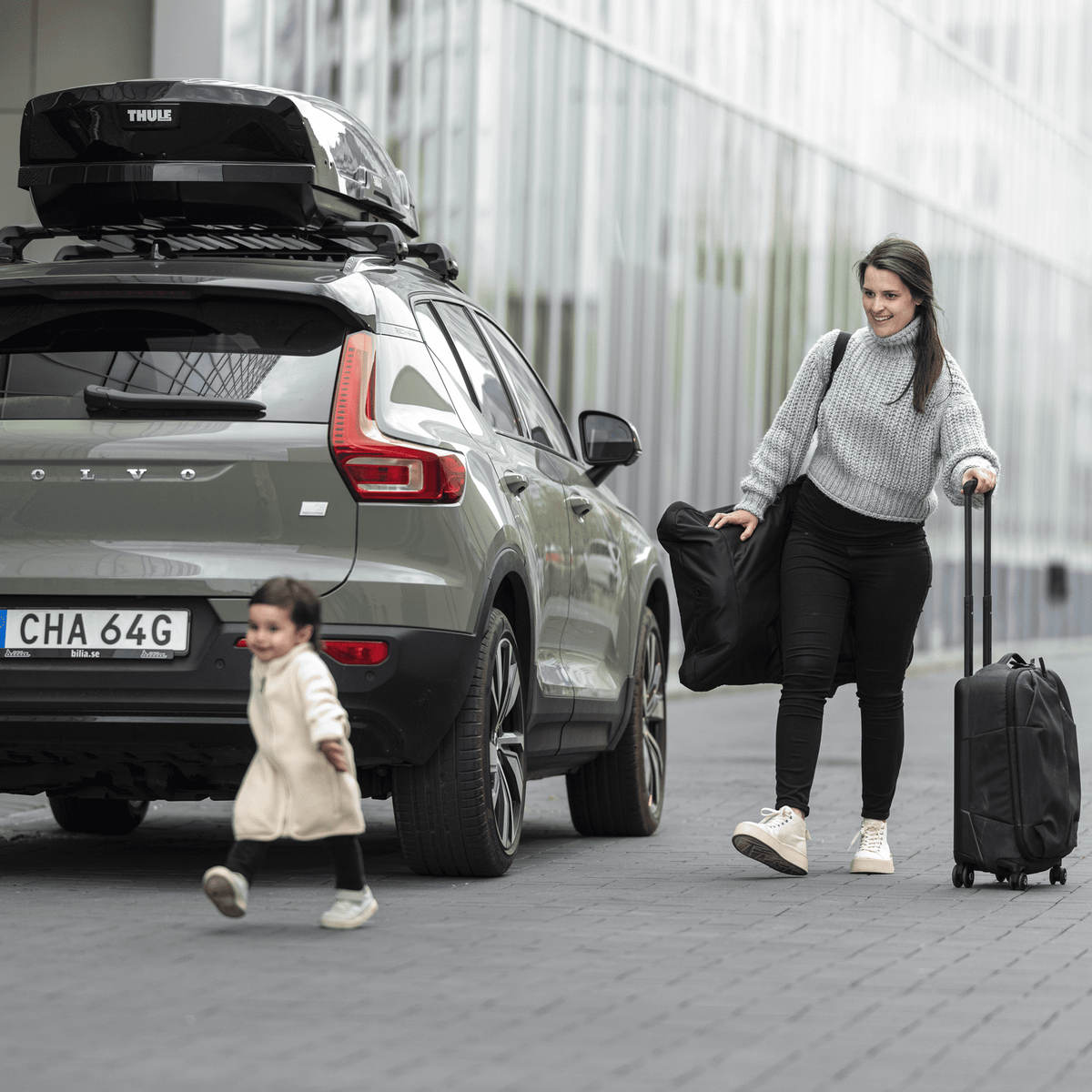 A mother and her child is walking past a parked car with a Thule Motion XT roof box.