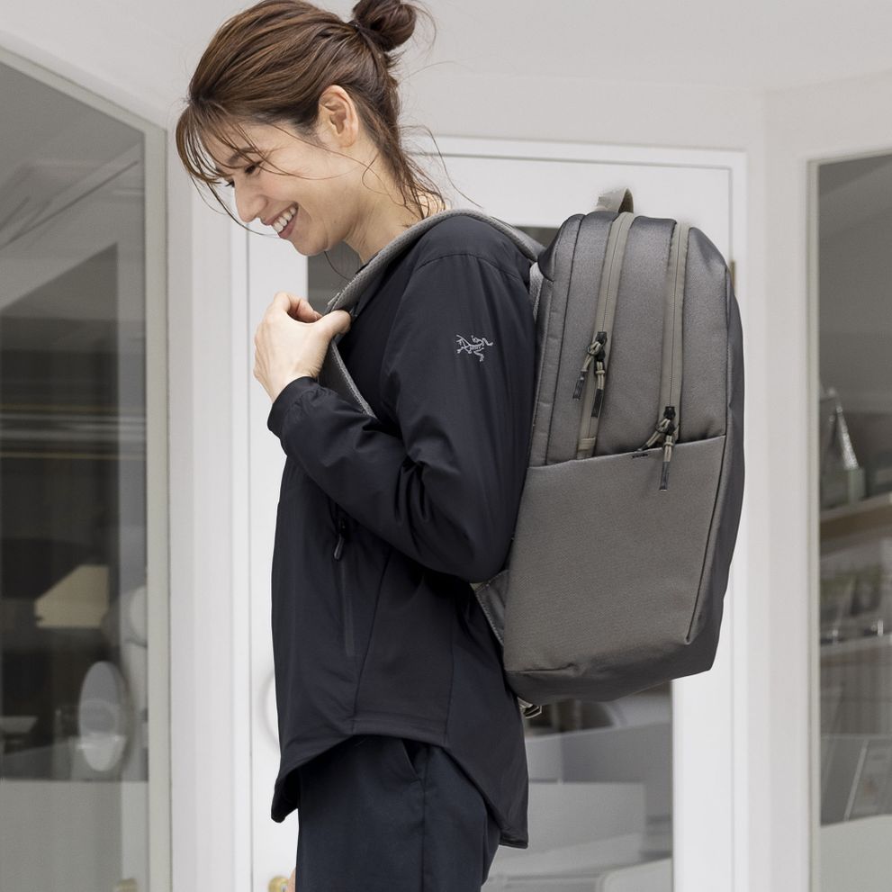 A woman wearing all black laughs, carrying a gray Thule Subterra backpack.