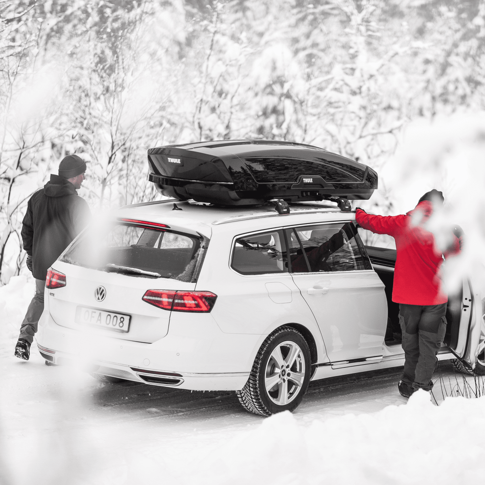 A couple is entering a car with a Thule Motion XT roof box.