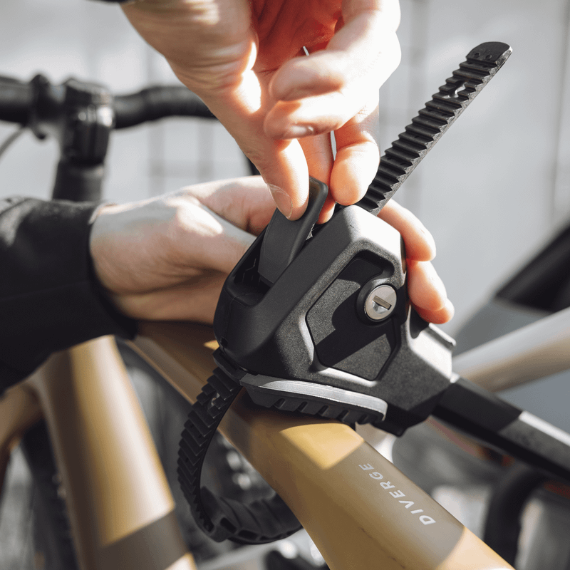 Close-up of a person fastening a bike to a rack using a secure strap mechanism on the frame of the bicycle.