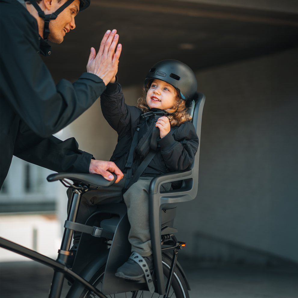 Parent giving a high-five to a smiling child seated in the Thule RideAlong 2 bike seat.
