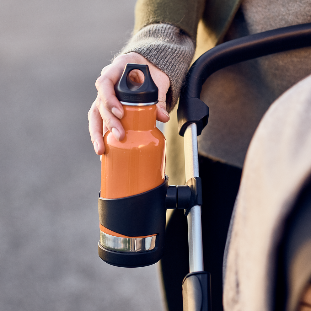 A close-up of a hand placing an orange thermos into the Thule Sleek Cup Holder.