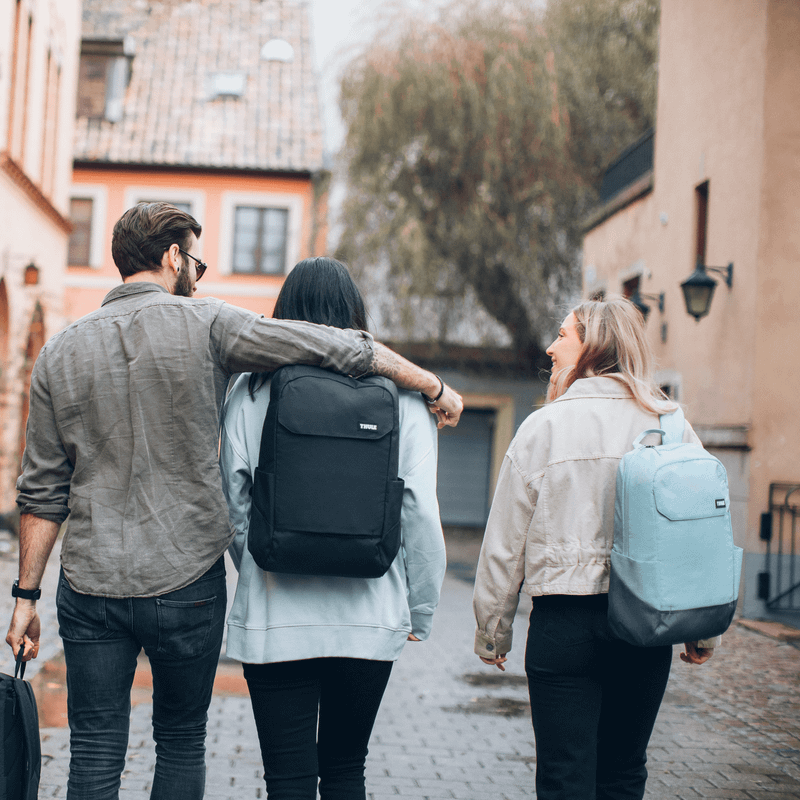 Four friends walk down a colorful, cobbled street carrying Thule Lithos backpacks.