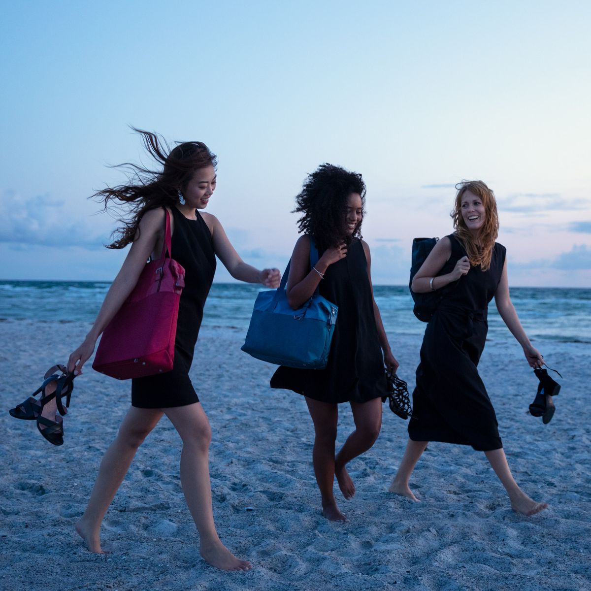 Three women walk on the beach  carrying Thule Spira weekender bags.