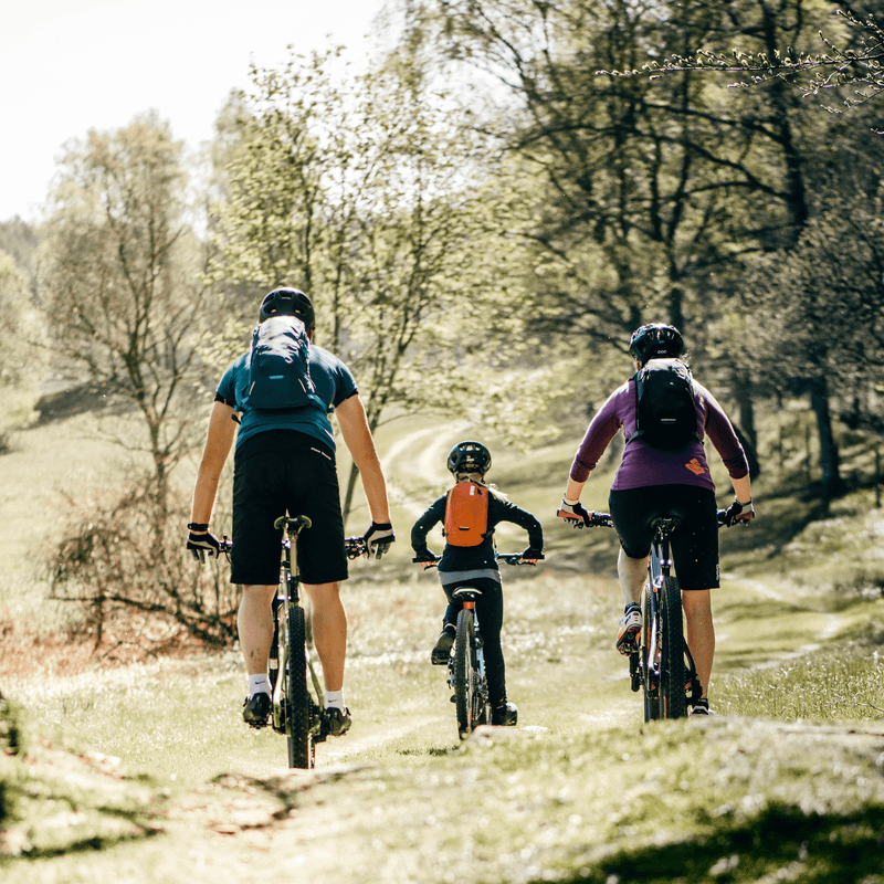 Three people go mountain biking through the woods with Thule Uptake hydration backpacks.