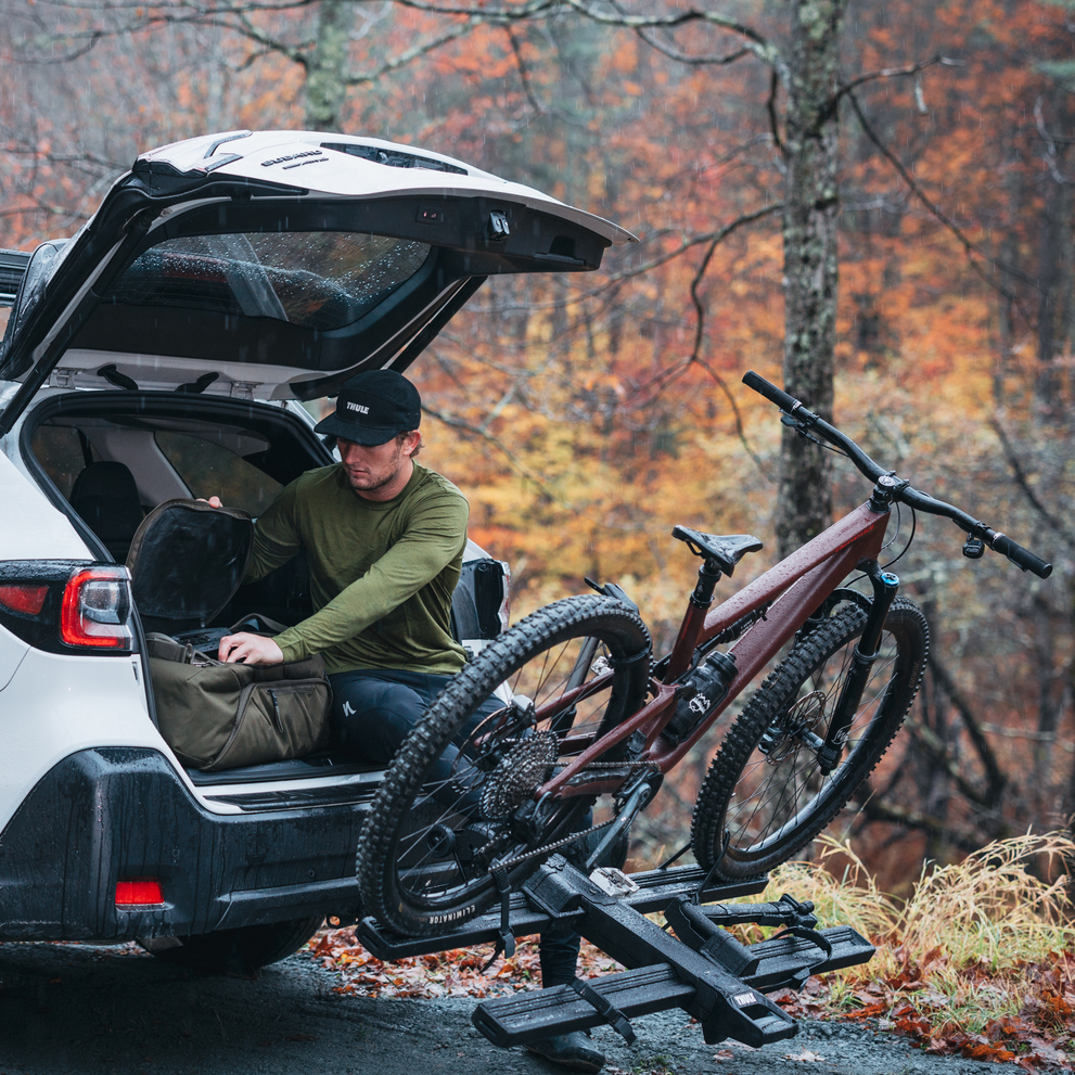 A man is sitting in the boot of a carwith the trunk open and the Thule Vero hitch bike rack is tilted down on the back of the car.