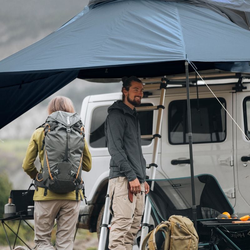 A man and a woman is standing under the awning of a roof top tent