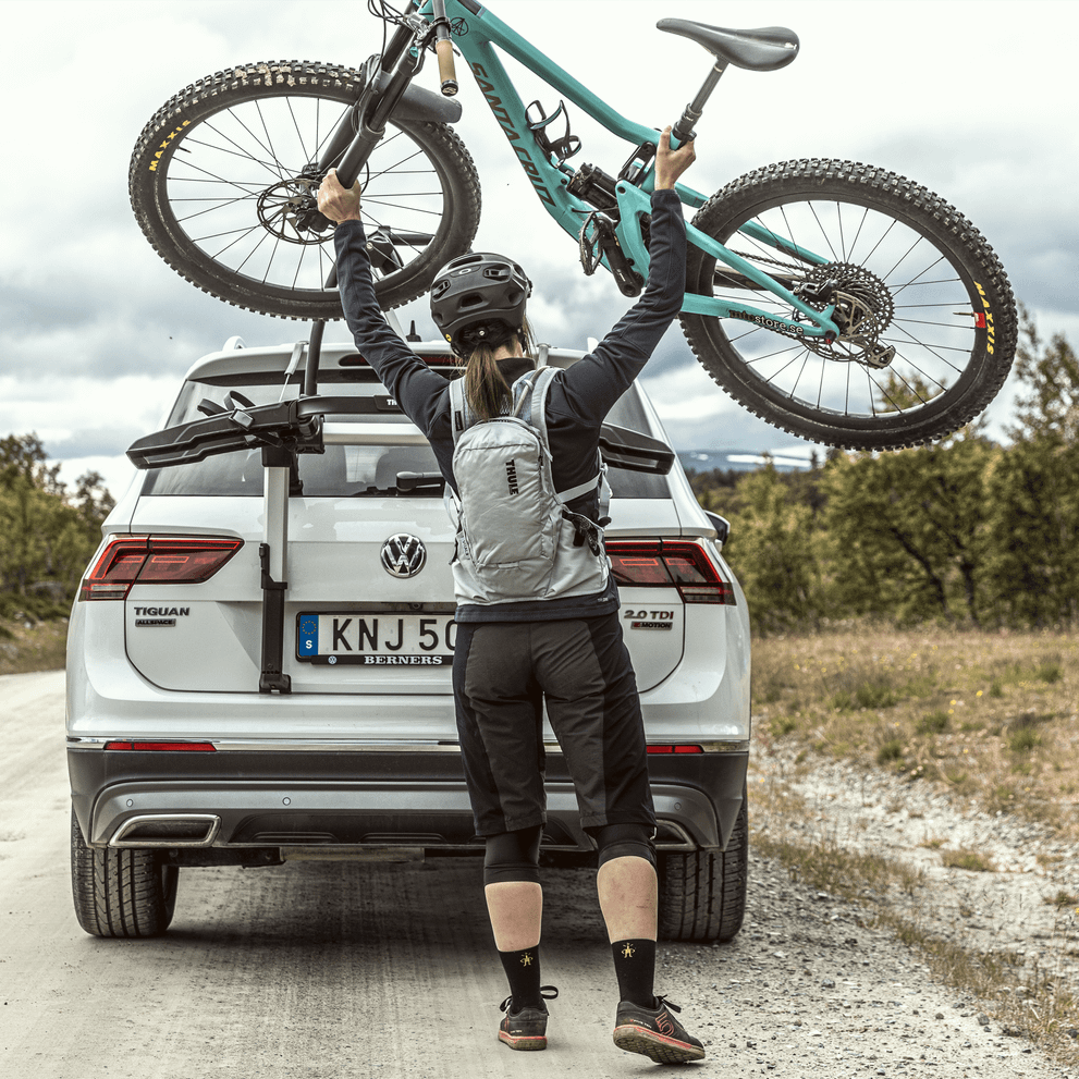 A cyclist loads her bike into a Thule Outway platform trunk bike rack in the countryside.