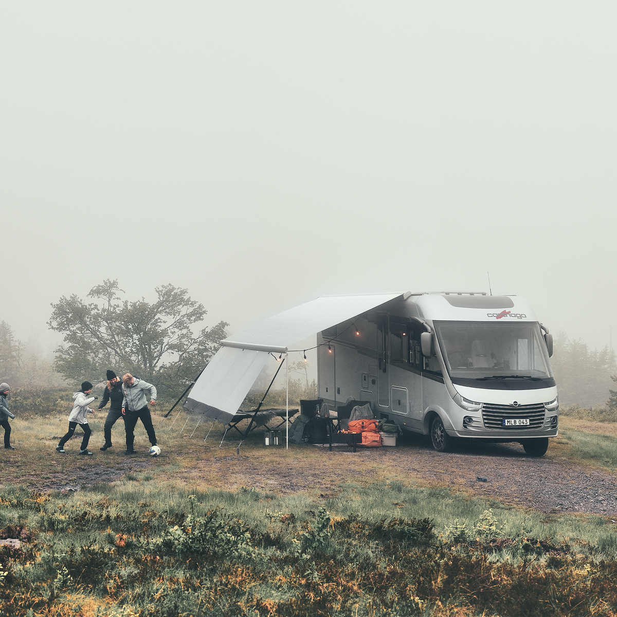 A family play football next to a motorhome with a Thule Omnistor 9200 RV awning on a cloudy day.
