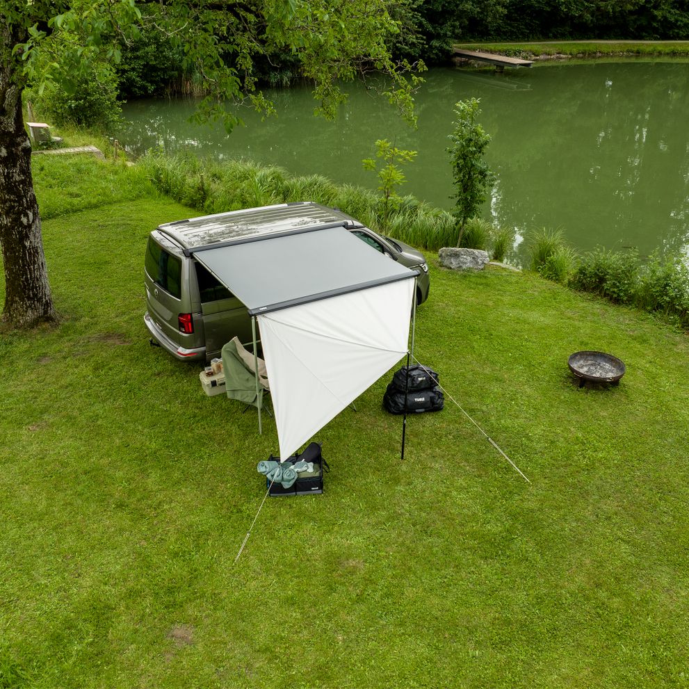 A van is parked next to the water with the Thule Subsola versatile awning panels.
