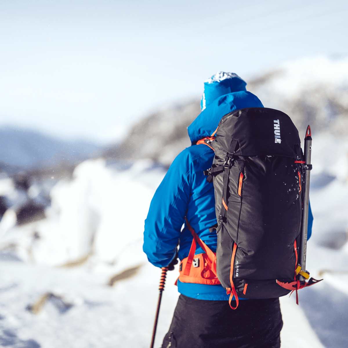 A man stands in the snowy mountains carrying a Thule AllTrail 45L backpack.