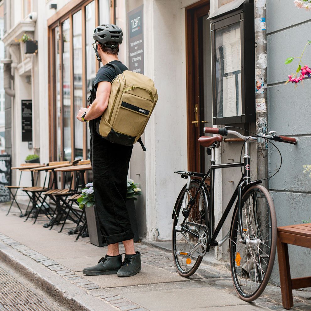 A man carries a beige Thule Paramount bike pannier standing outside a coffee shop.