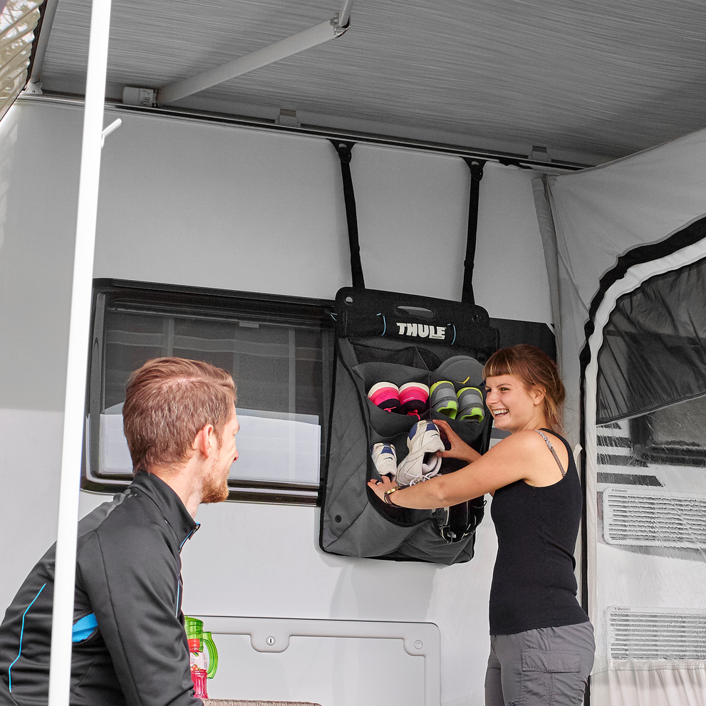 A woman loads shoes inside a Thule Shoe Organizer attached on a white caravan.