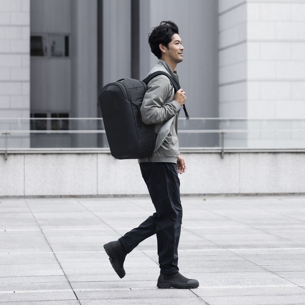 A man walks down a city street carrying a Thule Subterra backpack.