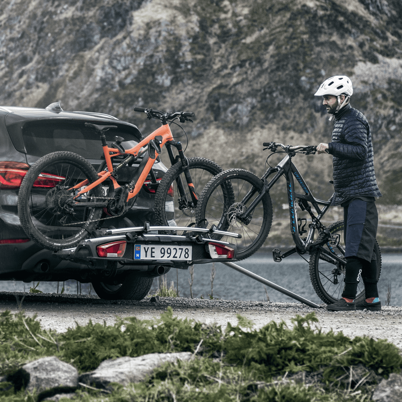 A cyclist loads their bike into a towbar bike rack with a Thule VeloSpace XT Bike Adapter.