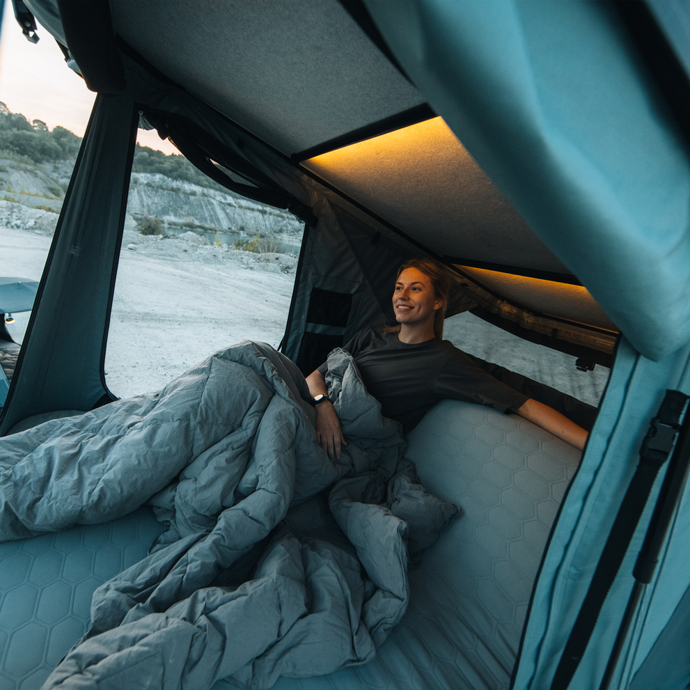A woman is sitting in the Thule Widesky hardshell rooftop tent built-in sofa enjoying the view.