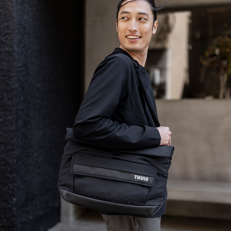 A man stands outside a cafe with a black Thule Paramount 14L messenger bag.