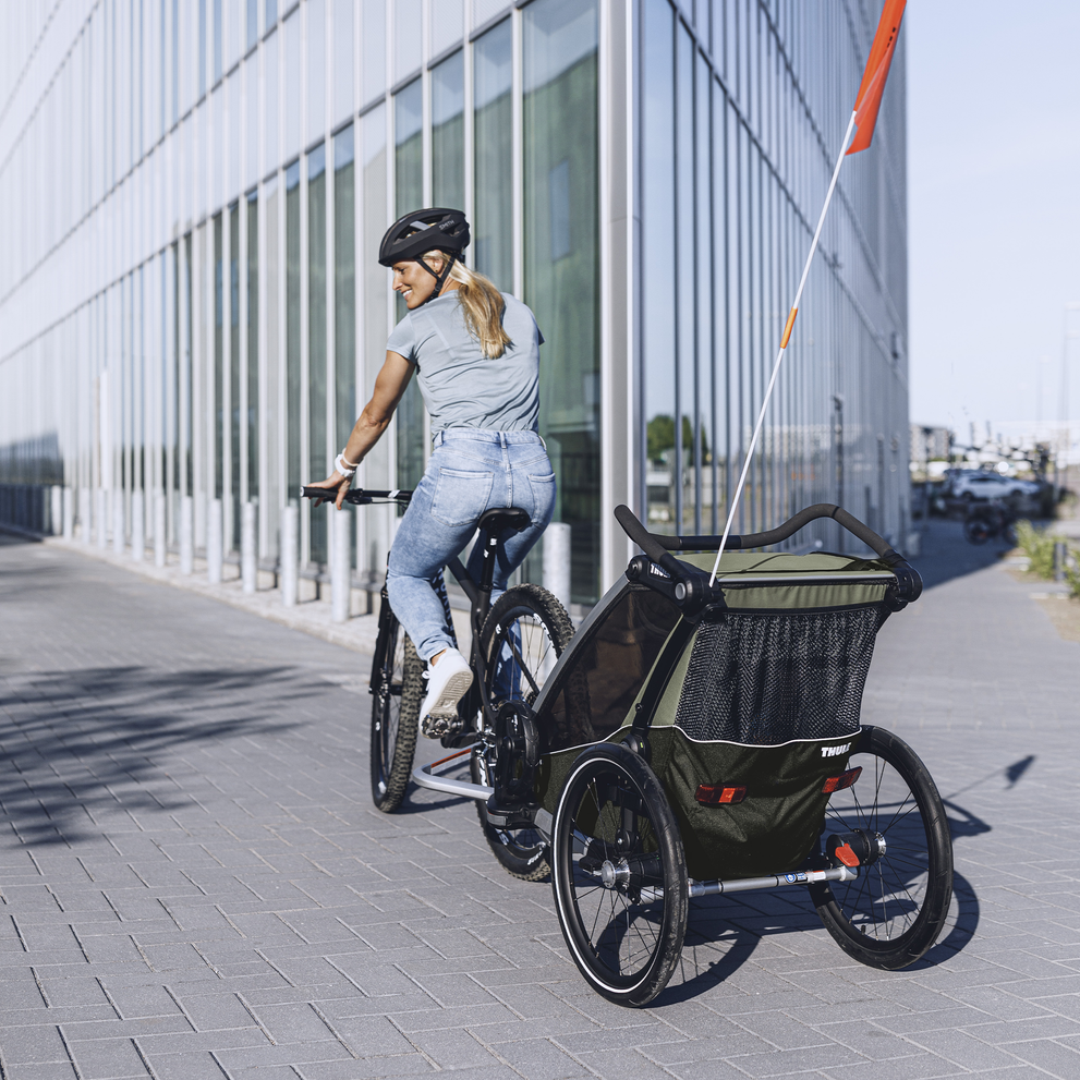 A woman bikes down a street with her child in the Thule Chariot Lite child bike trailer.