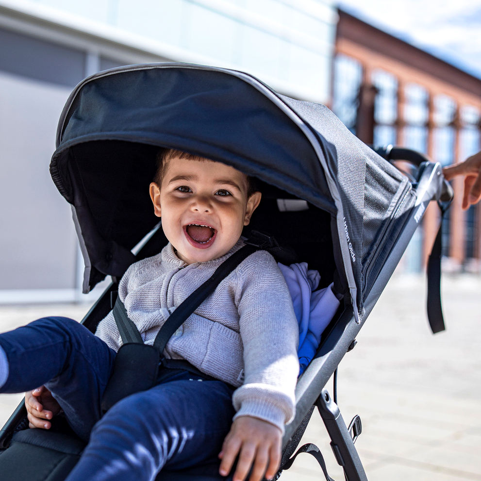 A close-up of a smiling toddler inside a blue Thule Urban Glide 2 all-terrain stroller.