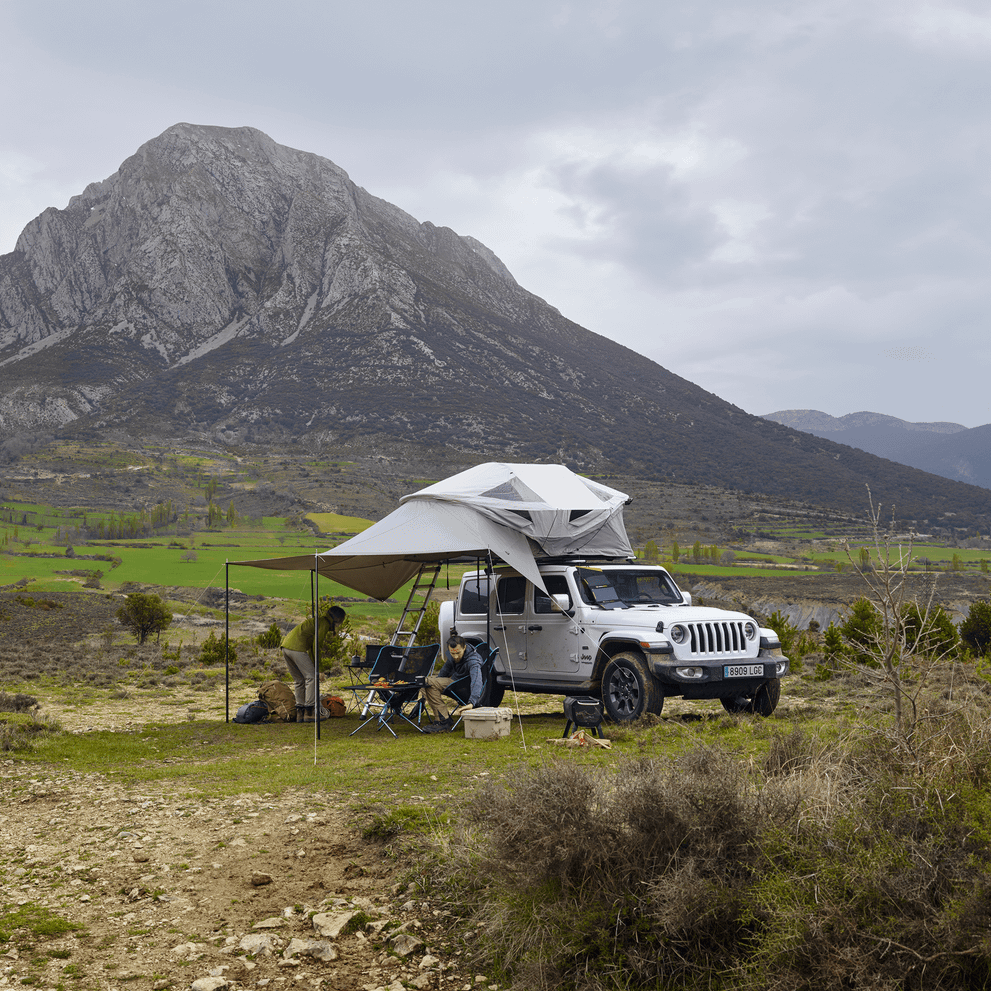 A car with a roof top tent and an awning is parked in front of a mountain