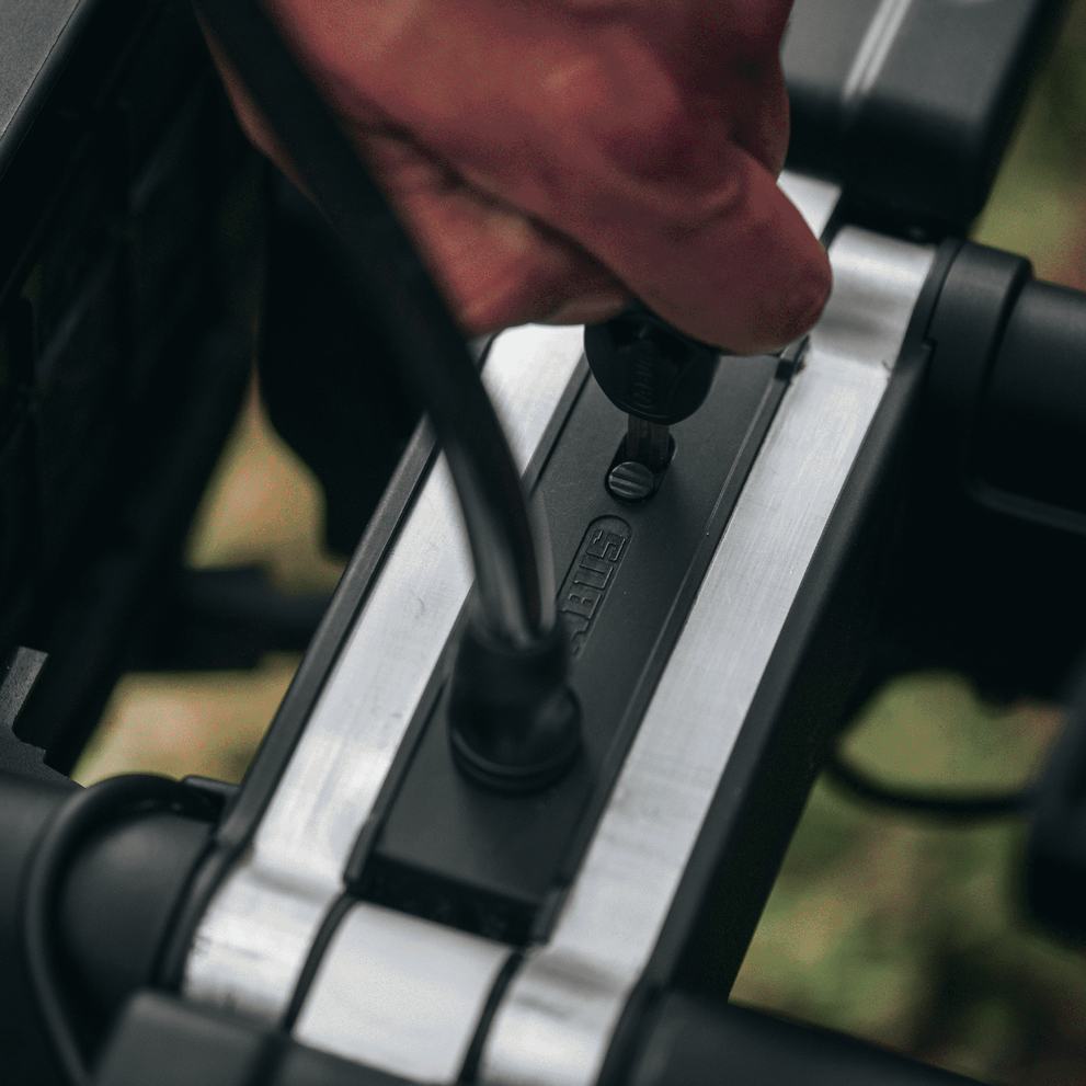 A close-up of a hand turning the key to the locking mechanism of a Thule High Grade Lock