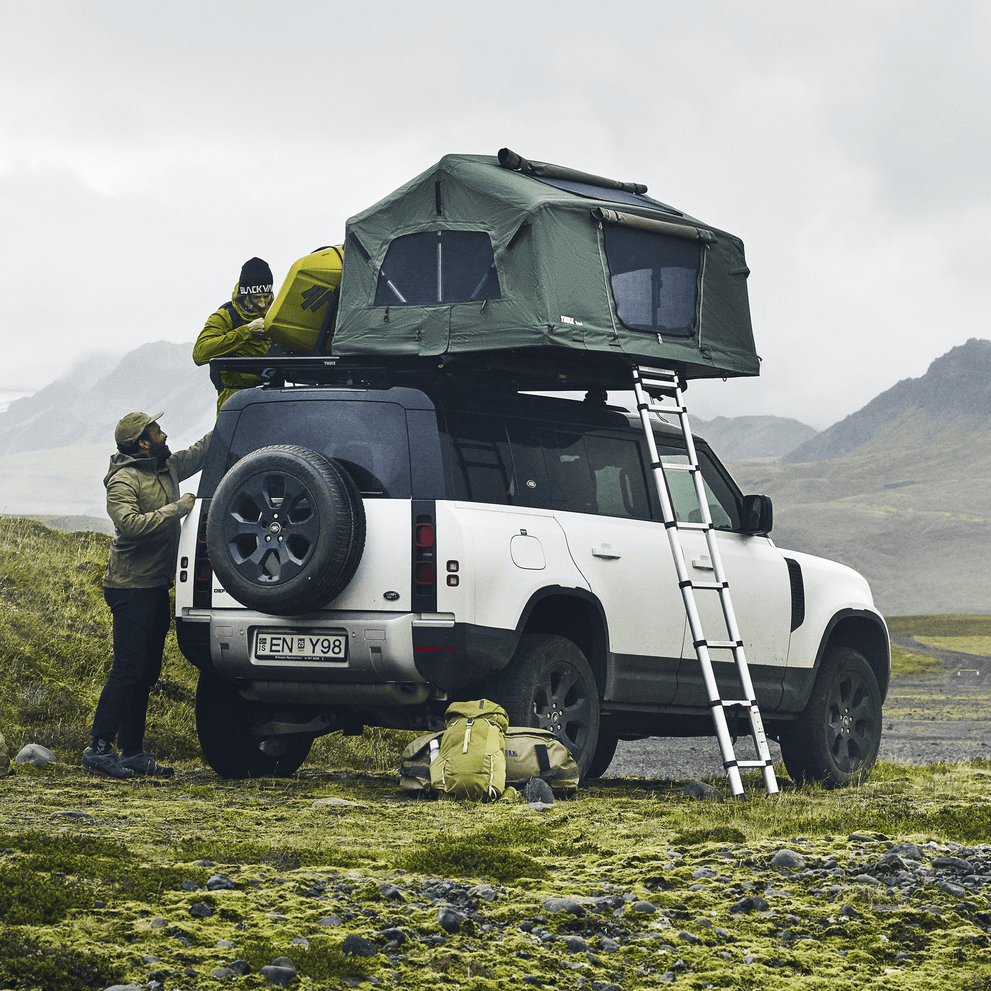 A vehicle is parked with a rooftop tent and a Thule Caprock roof rack platform.