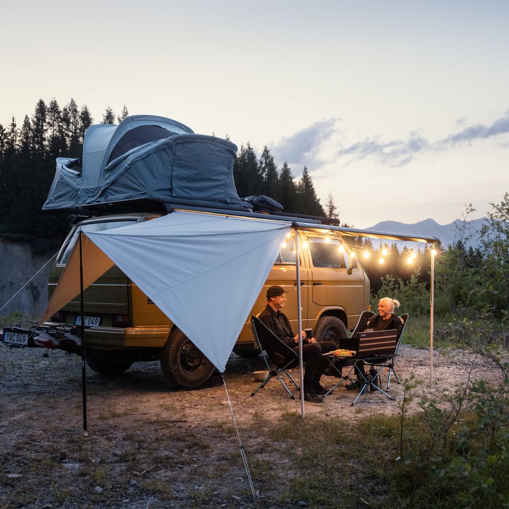 A van is parked in the sand with a rooftop tent and Thule Subsola van awning panels.