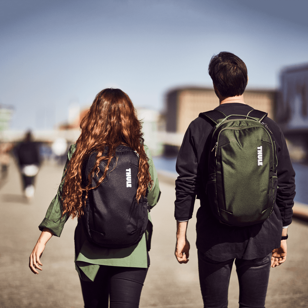 Two people walk down a sunny street carrying Thule Subterra Backpacks.