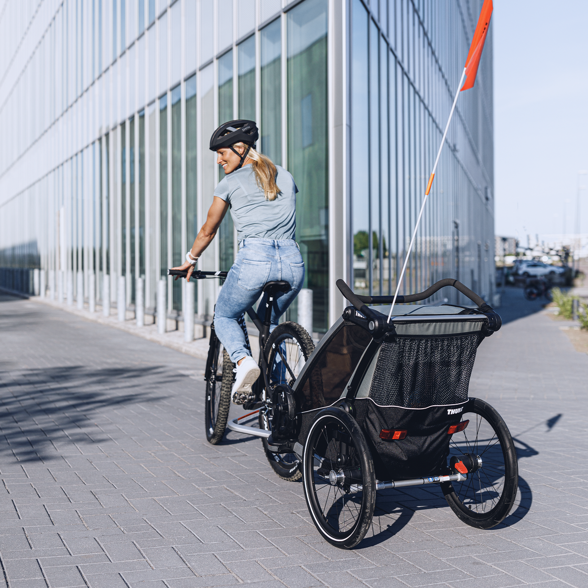 A woman bikes down a street with her child in the Thule Chariot Lite child bike trailer.