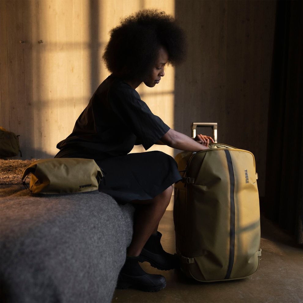 Woman packing a Thule Aion rolling suitcase sitting on a bed with a matching bag.