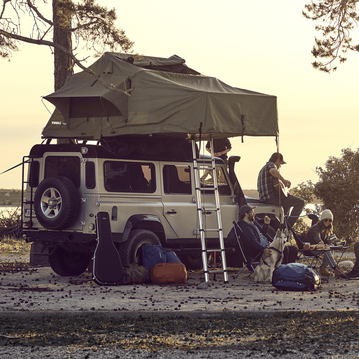 A group of people are standing in a forest beside a car with a Thule rooftop tent.