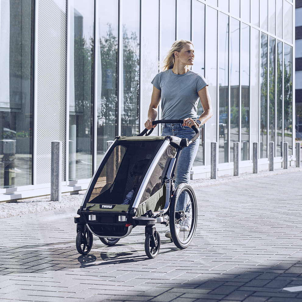 A woman strolls down a city street with her Thule Chariot Lite kids' bike trailer.