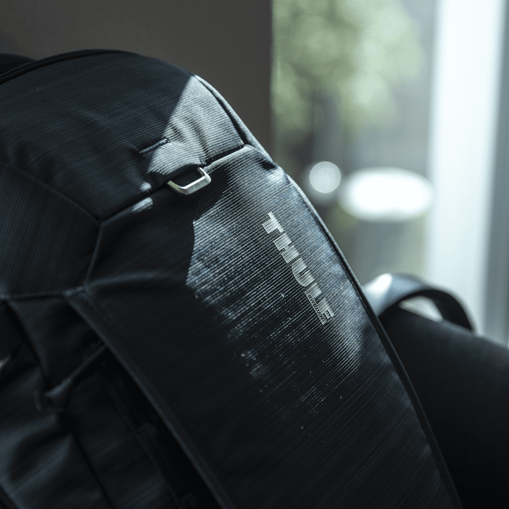 Details of the blue Thule Construct backpack with sun streaming in through the window in the background.