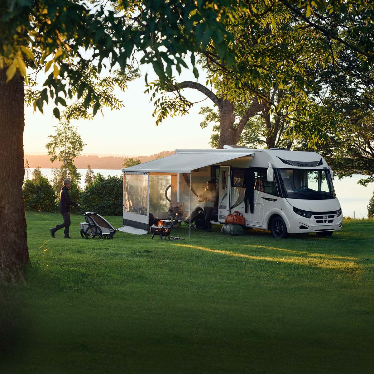 A motorhome is parked in the grass with a Thule Rain Blocker Front awning side wall.