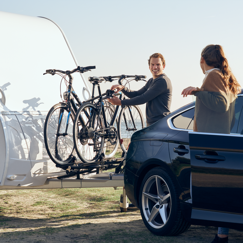 Two people unload bikes from a Thule Caravan Superb XT Black caravan bike rack.