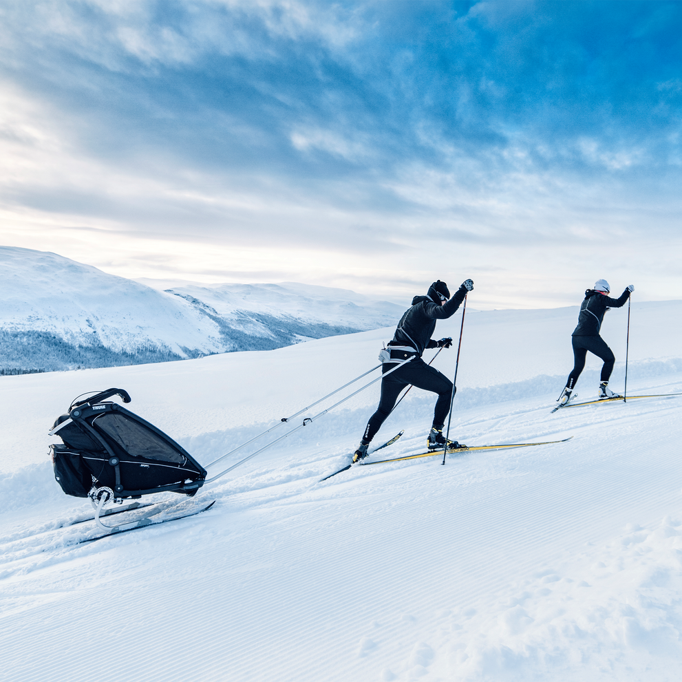 A couple goes cross-country skiing with the Thule Chariot child bike trailer using the Thule Chariot Ski Kit.