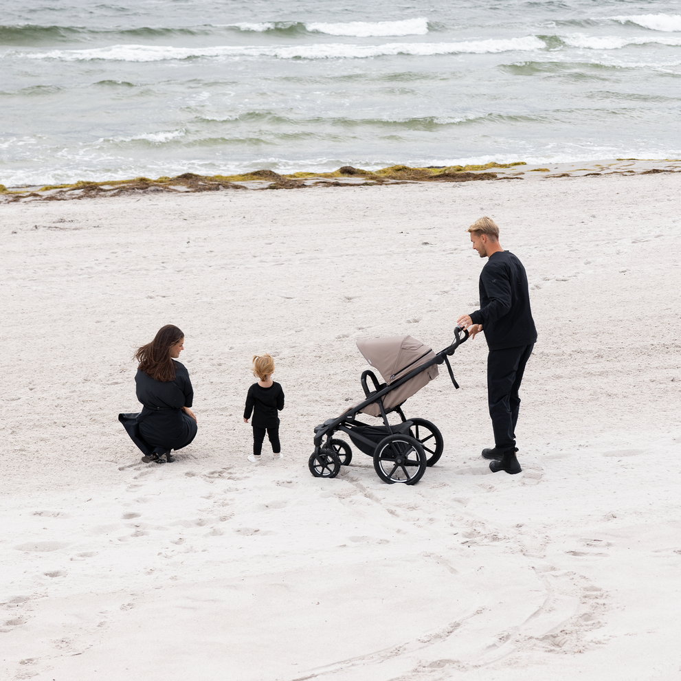 Famiglia sulla spiaggia con passeggino Thule Urban Glide a 4 ruote.