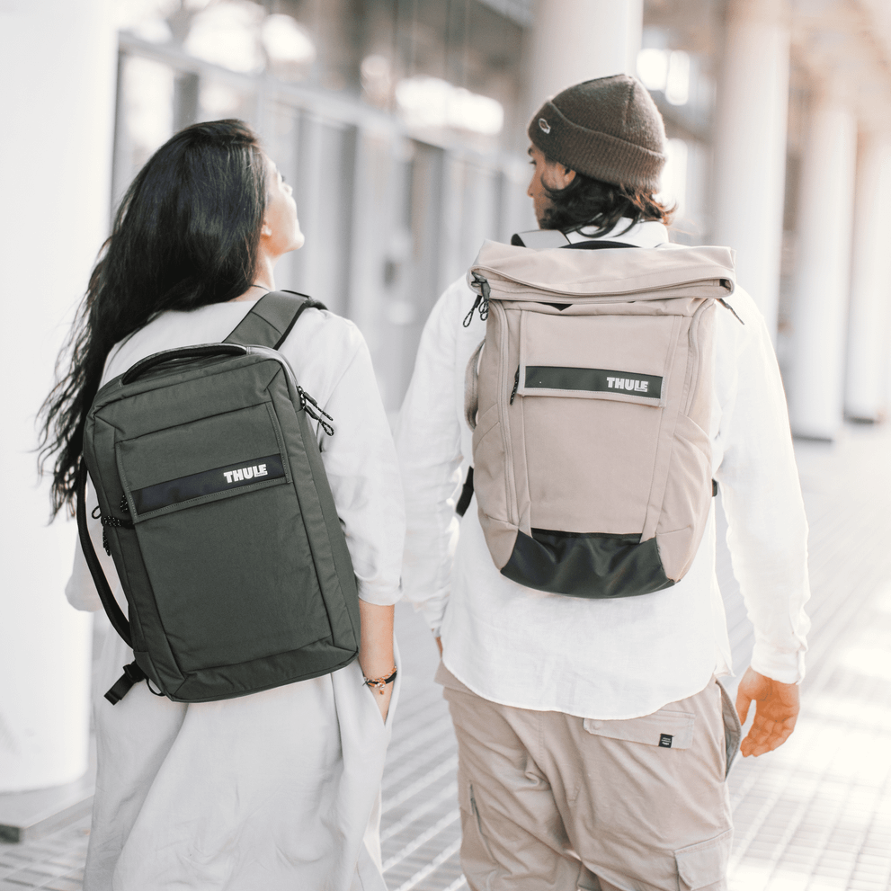 Three people walk down a sunny, glassy hallway carrying Thule Paramount Convertible laptop bags.