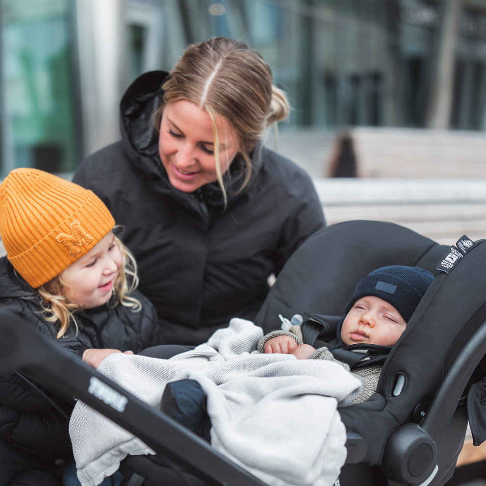 A woman looks at her baby inside a car seat using the Thule Urban Glide 2 Car Seat Adapter