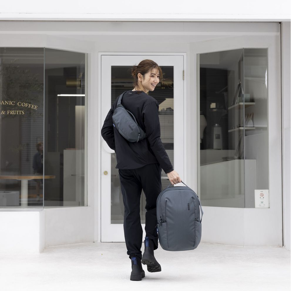 A woman enters the door of a building with the Thule Subterra sling and bag.
