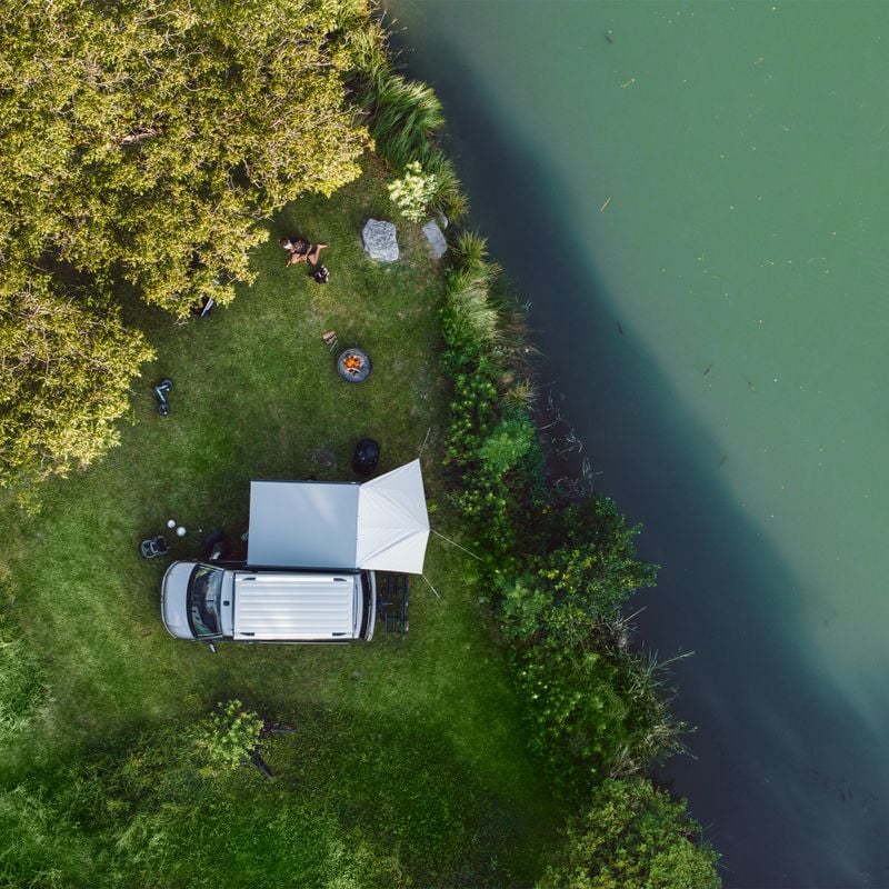 A vehicle is parked by the water with a Thule Subsola awning panel and awning.