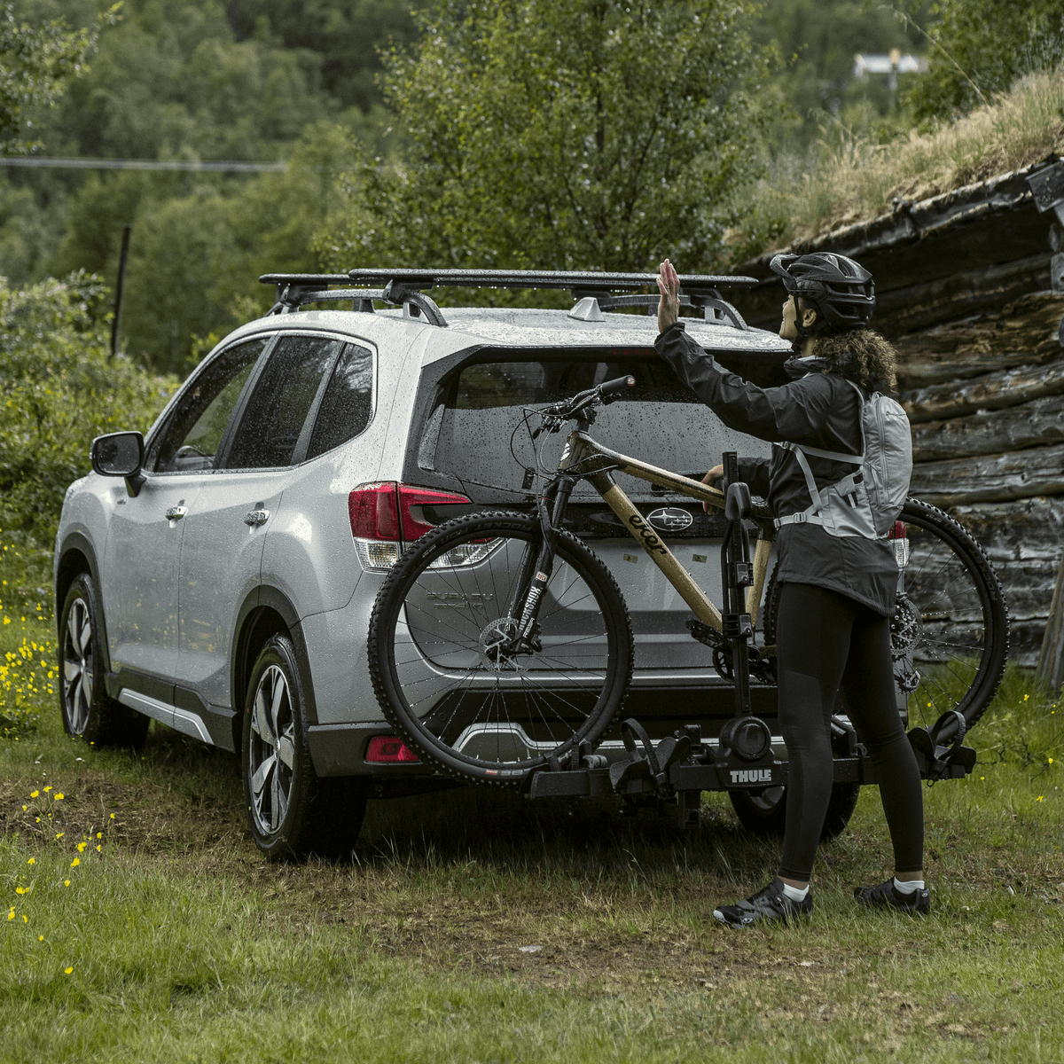 A car with a bike carrier is parked in front of a cottage.