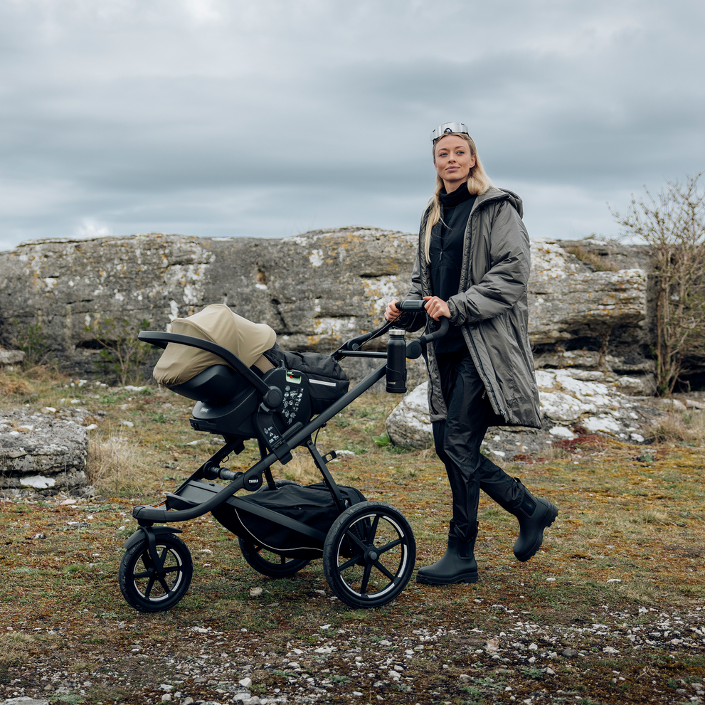 Adult pushing a stroller with a Thule Maple Connect infant car seat attached to it outdoors.