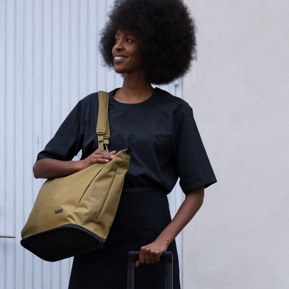 Person carrying a Thule Aion sling and rolling suitcase.
