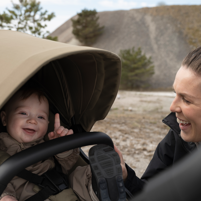Adult smiling at a child seated in a Thule Charm stroller outdoors.