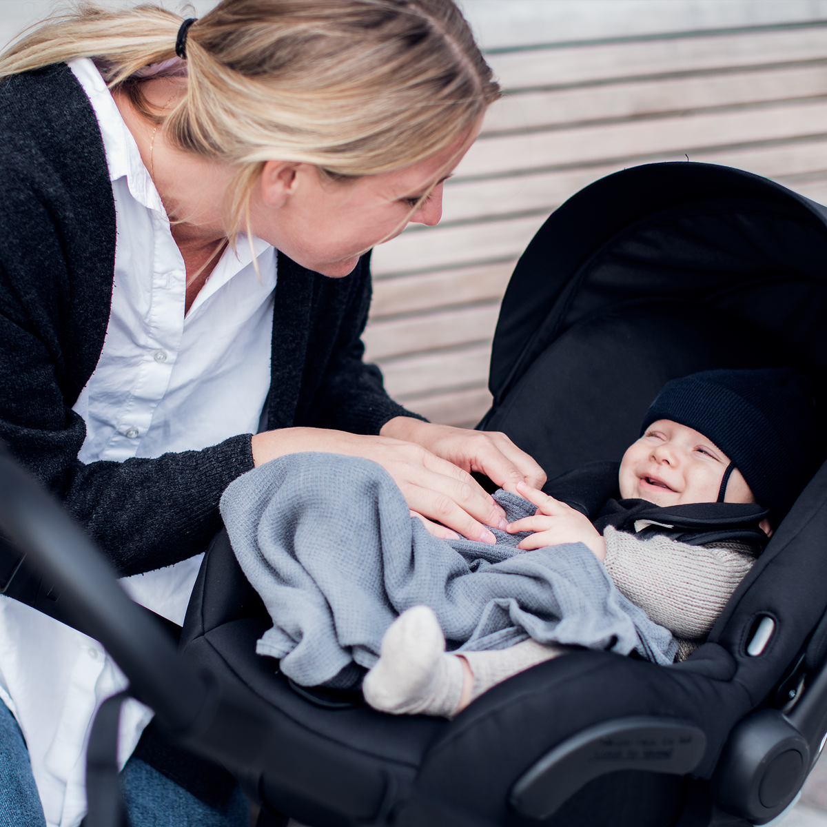 A woman looks at her baby in a car seat with a Thule Shine Car Seat Adapter.