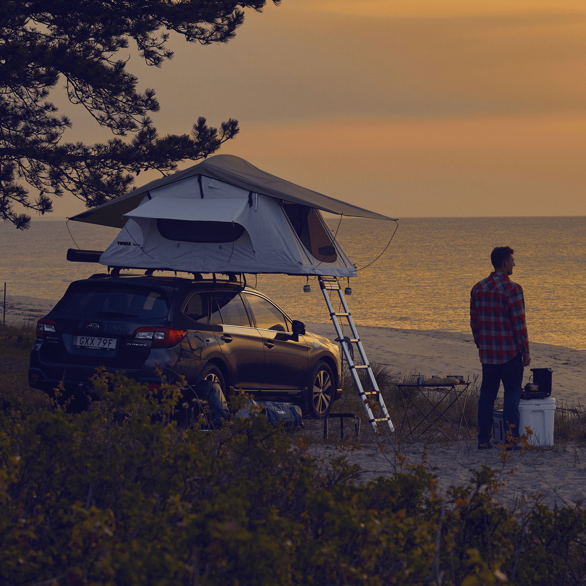 A man is looking at the sunset standing close to a car with a rooftop tent