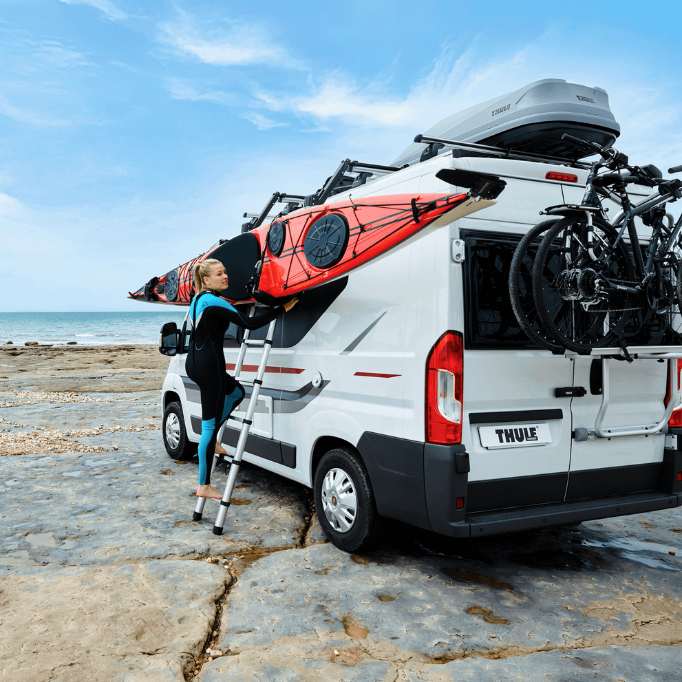 A woman is unloading a kayak on the roof of a van with a Thule Hullavator Pro